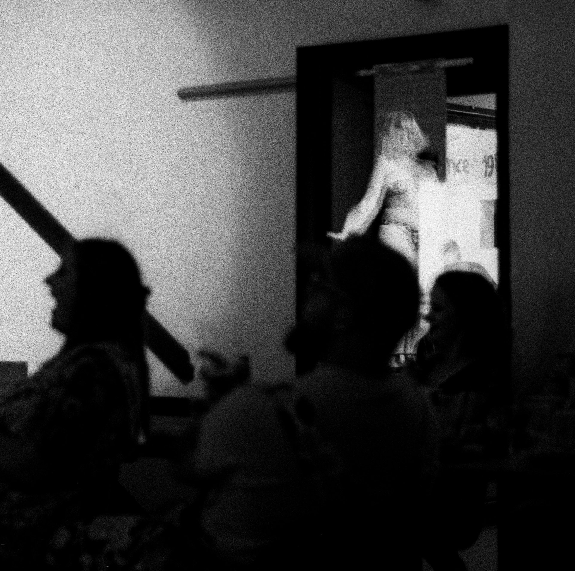A grainy black-and-white photograph shows two silhouetted figures in a dim interior, while a brightly lit figure stands in a doorway behind them.